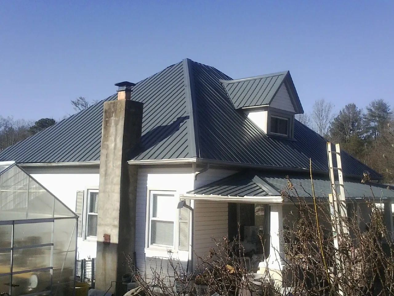 Dark blue standing seam metal roof on a white farmhouse with dormer — Slate & Tile Roof Repair by Roofing Brothers in Neenah