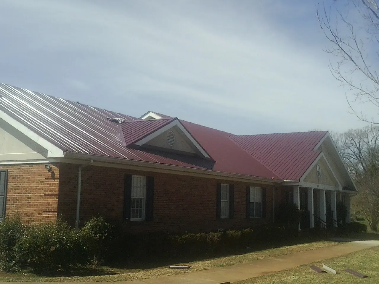 Red metal roof with gabled entries on a long brick building, from a Hail Damage Roof Repair job in Neenah