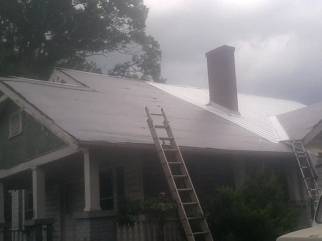 Ladders against a metal roof on an older home with a brick chimney in Neenah