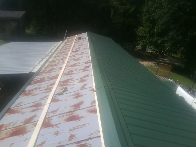 Old rusted panels beside newly installed green metal roofing — Wind Damage Roof Repair by Roofing Brothers in Neenah