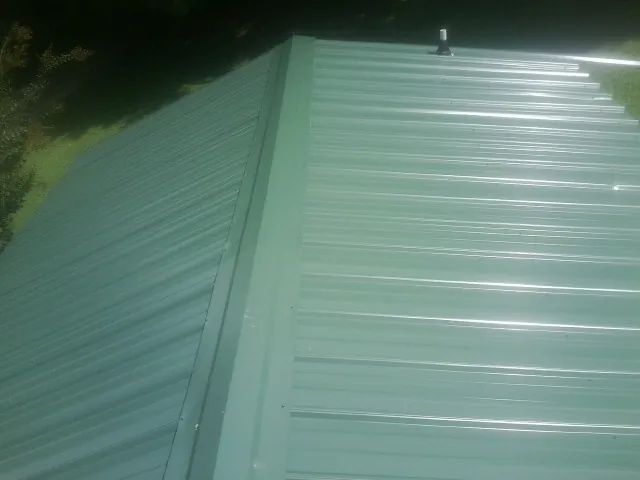 New green metal panels meeting at the ridge of a roof — Flat Roof Repair work by our crew in Neenah
