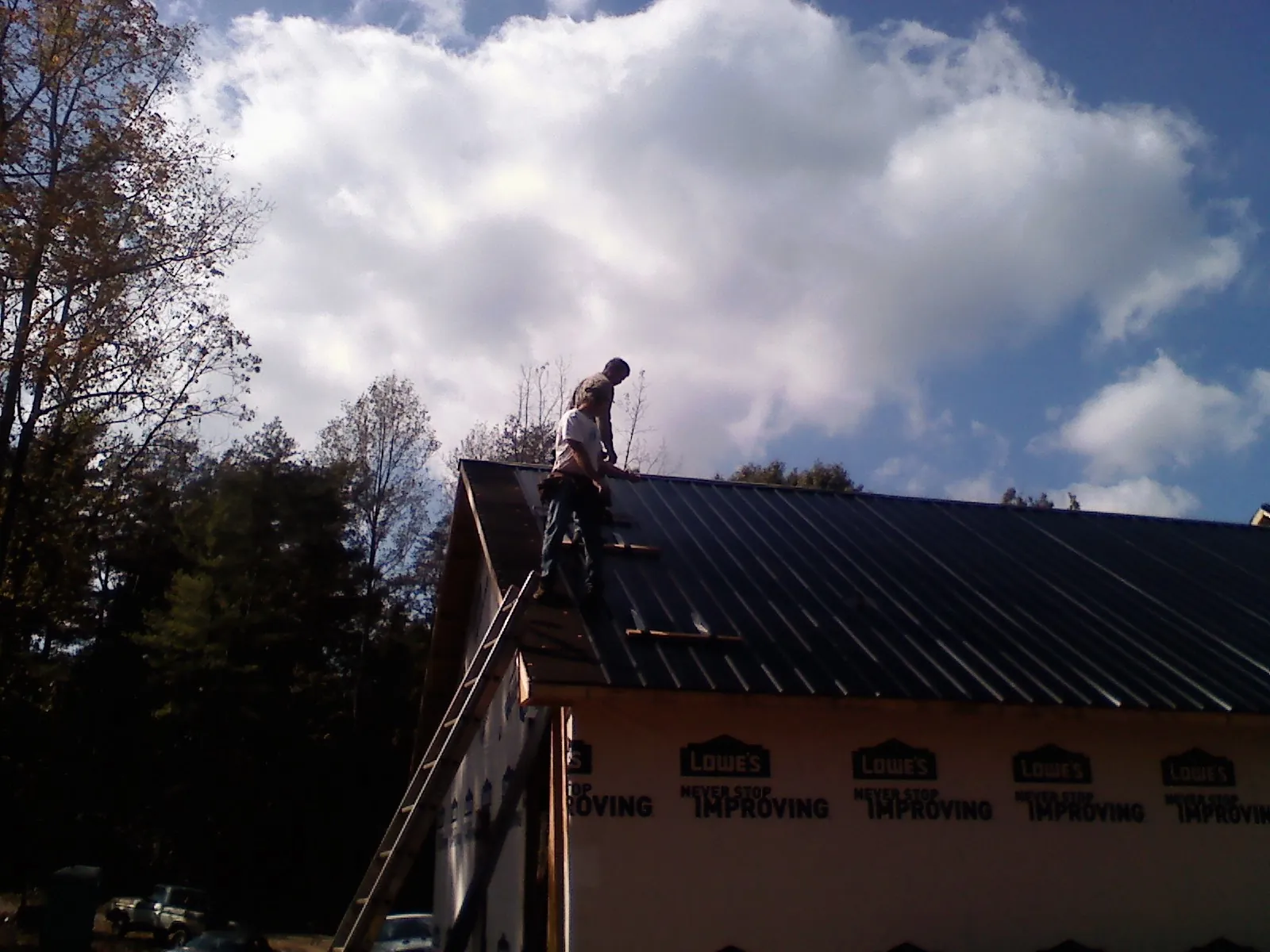 Roofer fastening dark metal panels high against a cloudy sky, from a Roof Inspection job in Neenah
