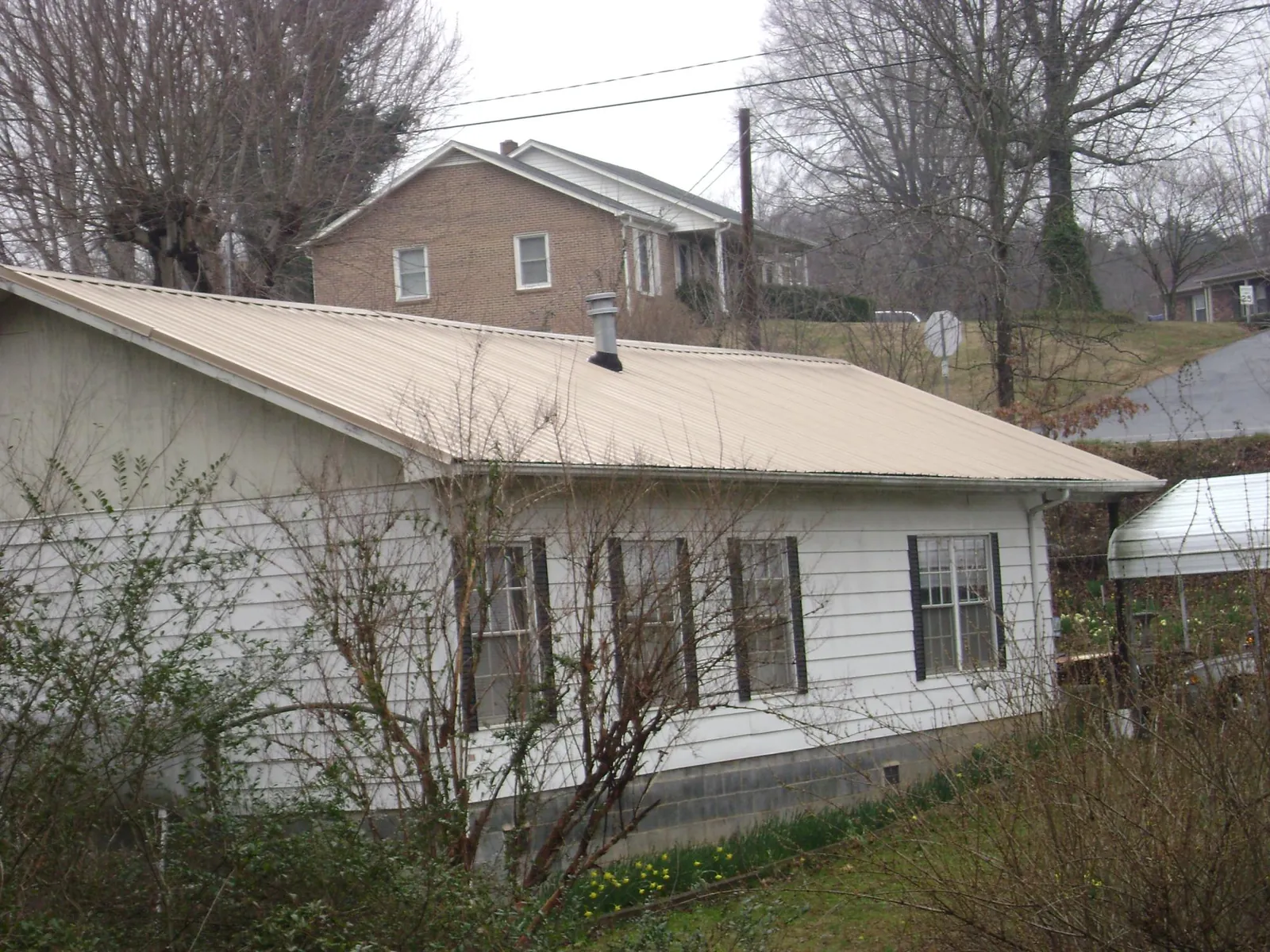 Tan metal roof on a white sided house set into a hillside — Commercial Roofing by Roofing Brothers in Neenah