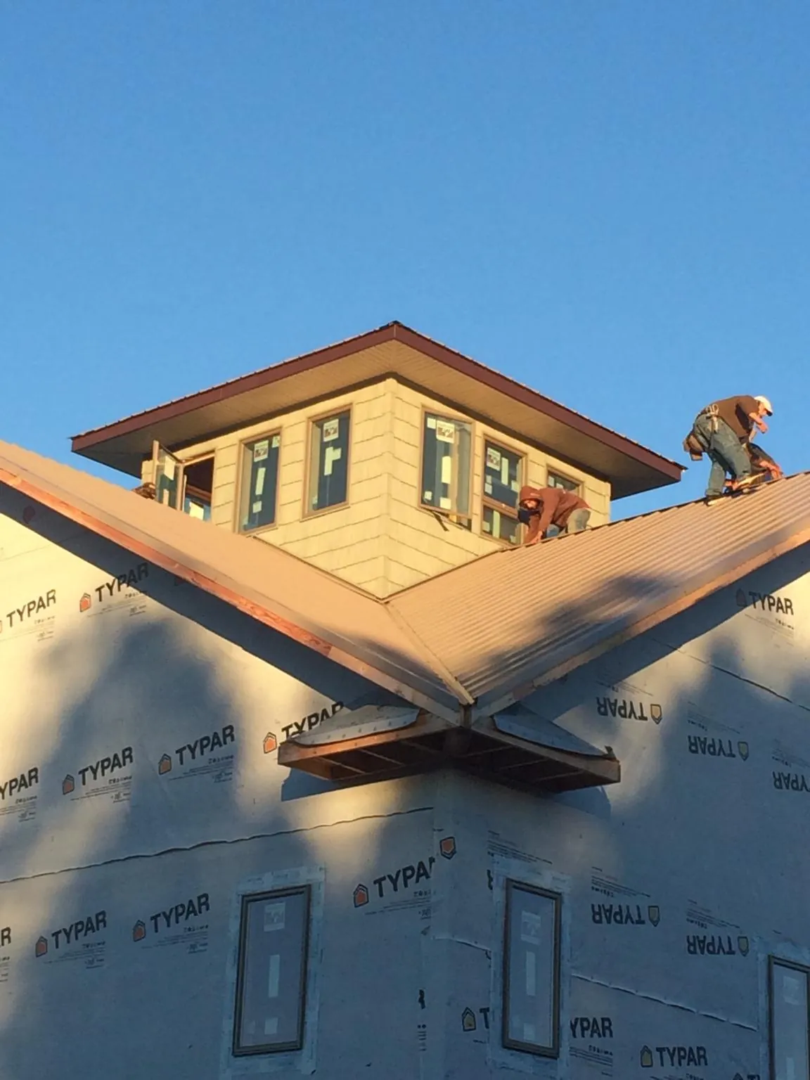 Roofers working around a rooftop cupola on a new metal roof at sunset — Roof Waterproofing in Neenah by Roofing Brothers